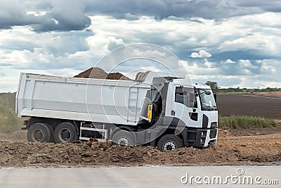 Dump truck with a bunch of land in the back at the construction site outside the city. Road works on an intercity highway Stock Photo