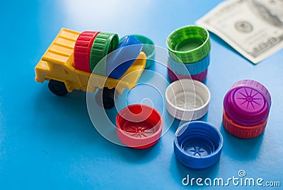 Dump truck with colored plastic bottle caps on blue background. 100 Dollars on table. Make money on Recycling Plastic, Bottles, Stock Photo
