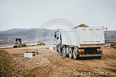 Industrial dumper trucks working on highway construction site, loading and unloading earth. heavy duty machinery activity Stock Photo