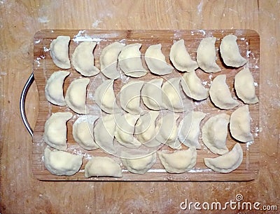 Dumplings with filling on a wooden board in flour. top view. raw frozen. traditional meal. Many dumplings on the Board in flour. Stock Photo