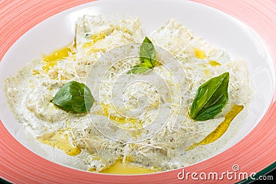 Dumplings with potatoes garnished with parmesan, cheese sauce, oil and basil on plate on black wooden background Stock Photo