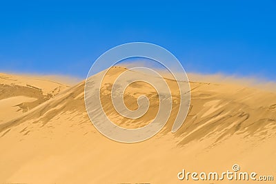 Dune against the background of a bright blue sky. The wind blows the sand off the ridge of the dune Stock Photo