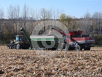 Challenger MT765D tractor pulling a Killbros 1820 grain cart being loaded from a Massy Ferguson 9540 combine harvester in norther Editorial Stock Photo