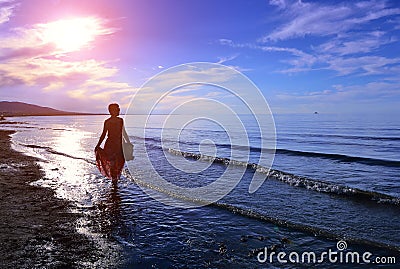 The setting sun, a woman walking on the beach Stock Photo