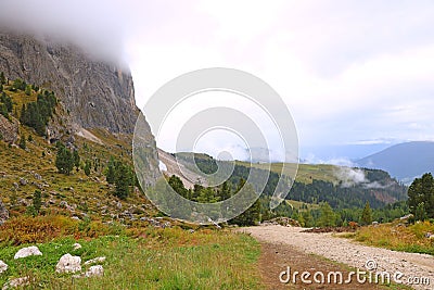 Dusty road leading to the peaks of the Dolomites covered with fog, gloomy sky background Stock Photo