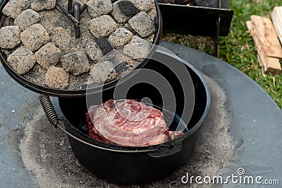Dutch oven camp cooking with coal briquettes beads on top, Meat lamb shoudler in the camp oven Stock Photo