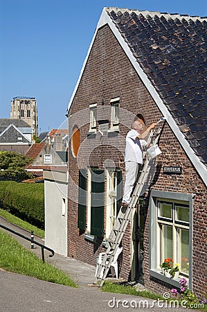 Dutch painter stands on ladder painting eaves Editorial Stock Photo