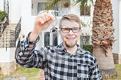 Dwelling, buying home, real estate and ownership concept - handsome man showing his key to new home Stock Photo