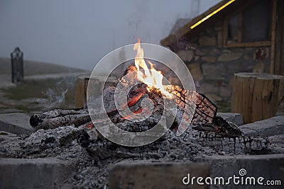 The dying fir.Thick smoke over the fire, in the background the stone wall of the house and the fog Stock Photo