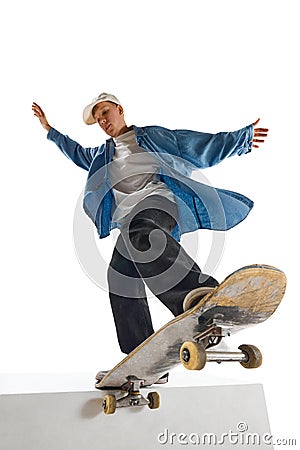 Dynamic image of teen boy in blue shirt and capo training, in motion, skateboarding over white background Stock Photo