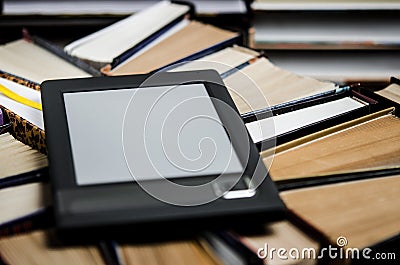 The e-book with a white screen lies on the open multi-colored books that lie on a dark background, close-up Stock Photo