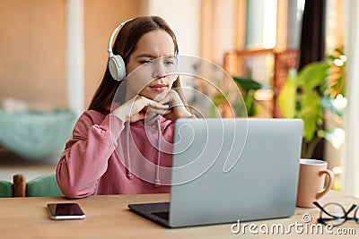 E-education, online lessons concept. Focused teen girl in headset looking at laptop screen, sitting at table at home Stock Photo