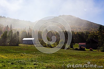 Early fall landscape with small cabins at the foot of mountains seen through a screen of smoke Stock Photo