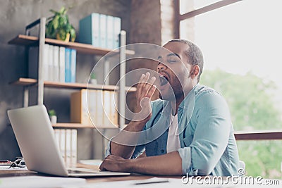 Early morning in the office. Sleepy tired freelancer is yawning at his work place in front of the laptop`s screen on desk top Stock Photo