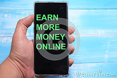 Earn more money online, text words typography written on smart phone against blue background, life and business motivational Stock Photo