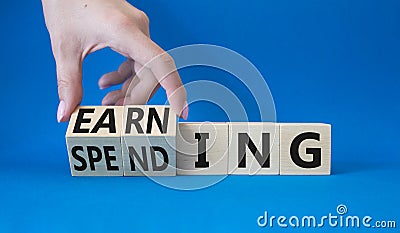 Earning and Spending symbol. Businessman hand. Turned cubes with words Earning and Spending. Beautiful blue background. Business Stock Photo