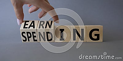 Earning and Spending symbol. Businessman hand. Turned cubes with words Earning and Spending. Beautiful grey background. Business Stock Photo