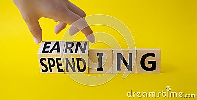 Earning and Spending symbol. Businessman hand. Turned cubes with words Earning and Spending. Beautiful yellow background. Business Stock Photo