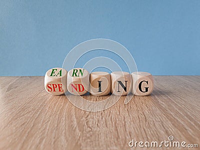 Earning or spending symbol. Turned cubes and changes red words spending to earning. Beautiful blue background. Copy space. Stock Photo