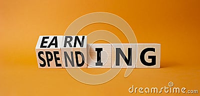 Earning and Spending symbol. Turned cubes with words Earning and Spending. Beautiful orange background. Business and Earning and Stock Photo