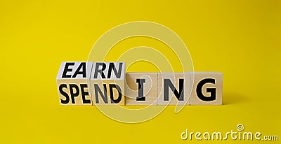 Earning and Spending symbol. Turned cubes with words Earning and Spending. Beautiful yellow background. Business and Earning and Stock Photo