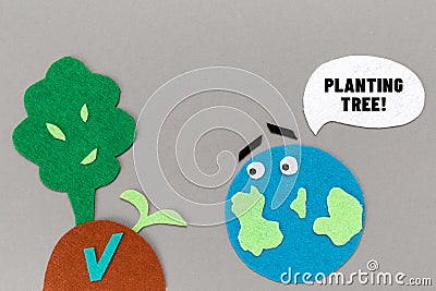 Earth Day. Cutted out of felt the planet Earth with emoticon and soil with a tree and plant sprout. Gray background. Flat lay. The Stock Photo