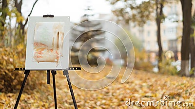 An easel with a finished picture standing in the autumn park, city and trees on background Stock Photo