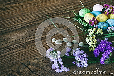 Easter background. Bright colorful eggs in nest with spring flowers over wooden dark background. Selective focus with Stock Photo
