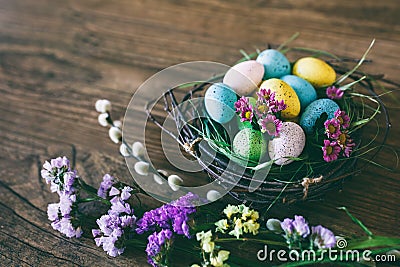 Easter background. Bright colorful eggs in nest with spring flowers over wooden dark background. Selective focus with Stock Photo