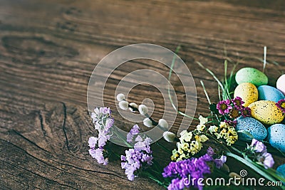 Easter background. Bright colorful eggs in nest with spring flowers over wooden dark background. Selective focus with Stock Photo