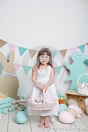 Easter! Beautiful little girl in a white dress with Easter eggs and a basket on a bright Easter scenery. Easter location, decorati Stock Photo