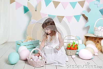 Easter! Beautiful little girl in a white dress lays Easter eggs in a basket. Many different colorful Easter eggs, colorful interio Stock Photo