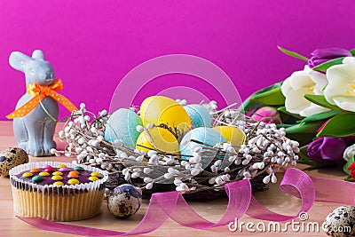 Easter blue and yellow eggs in the nest, cupcake, easter rabbit and tulips. Easter background with colorful tulips. Stock Photo