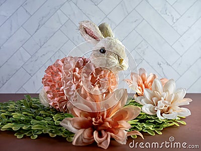 Easter Bunny Decor sitting on green leaves surrounded by peach artificial dahlia flower blooms, perfect for the spring holiday Stock Photo