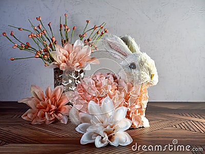 Easter Bunny Decor sitting on a wooden surface surrounded by peach artificial dahlia flower blooms, perfect for the spring holida Stock Photo