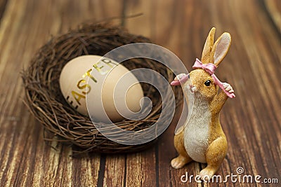 Easter bunny with a wicker nest and a wooden egg with a golden inscription Stock Photo