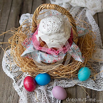 Easter cake - kulich.Traditional Easter sweet bread decorated white icing in straw basket and colored eggs on lace napkin on Stock Photo