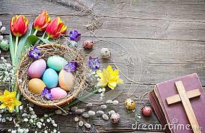 Easter colorful eggs in the nest with flowers on vintage wooden boards with bible and cross Stock Photo