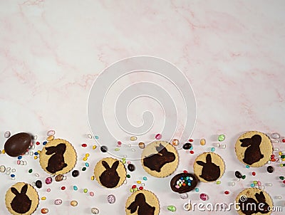 The border is made of homemade cookies with silhouettes of Easter bunnies and chocolate eggs on a pink marble background. Stock Photo