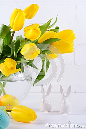 Easter composition with bouquet of yellow tulip flowers in glass vase and two white ceramic rabbits on white Stock Photo