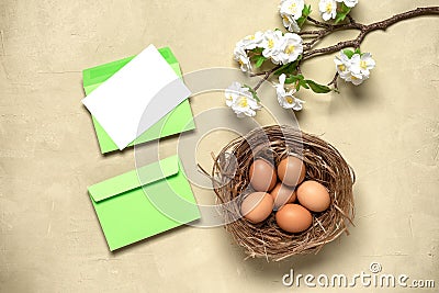 Easter composition. Brown eggs in the nest, cherry blossom branch artificial and mockup blank greeting card in an envelope. Stock Photo