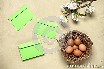 Easter composition. Brown eggs in the nest, sakura blossom branch artificial and green envelope. Concrete beige background. Top Stock Photo