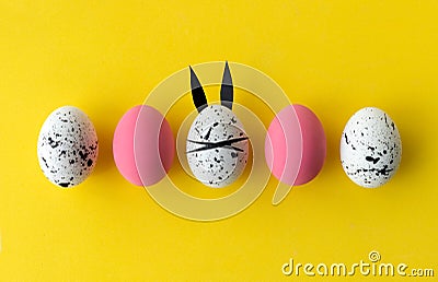 Easter composition with colored eggs and egg with bunny ears and face on yellow background Stock Photo