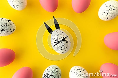 Easter composition with colored eggs and egg with bunny ears and face on yellow background Stock Photo