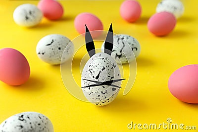 Easter composition with colored eggs and egg with bunny ears and face on yellow background Stock Photo