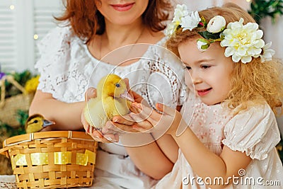 Easter composition. Mother and daughter in white dresses and flower wreaths on their heads play with ducklings. Farm village Stock Photo