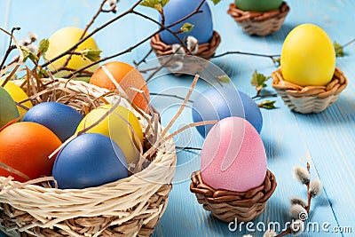 Easter composition - several colored eggs in a basket on a blue wooden table with willow twigs Stock Photo