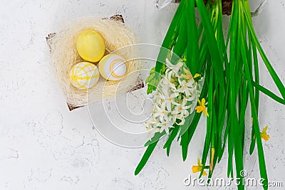 Easter concept. Yellow Easter eggs in a nest next to a bouquet of daffodils on a white concrete table. View from above Stock Photo