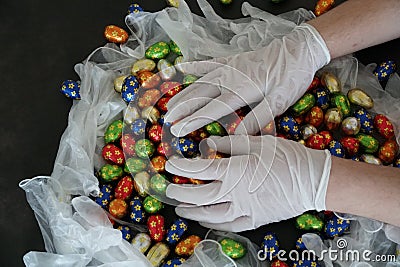 Easter in COVID-19 times, two hands in surgical gloves arrange small eater chocolate eggs Stock Photo