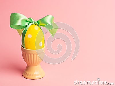 Easter creative concept. One yellow egg tied with a green ribbon standinng in the yellow egg cup a on a pink background. Stock Photo